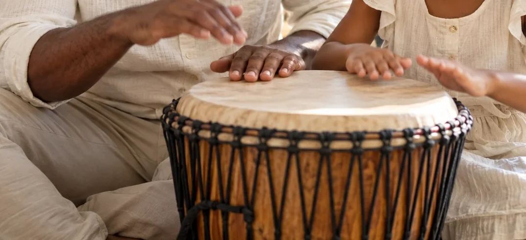 Two pairs of hands, one big and one small, on a djembe